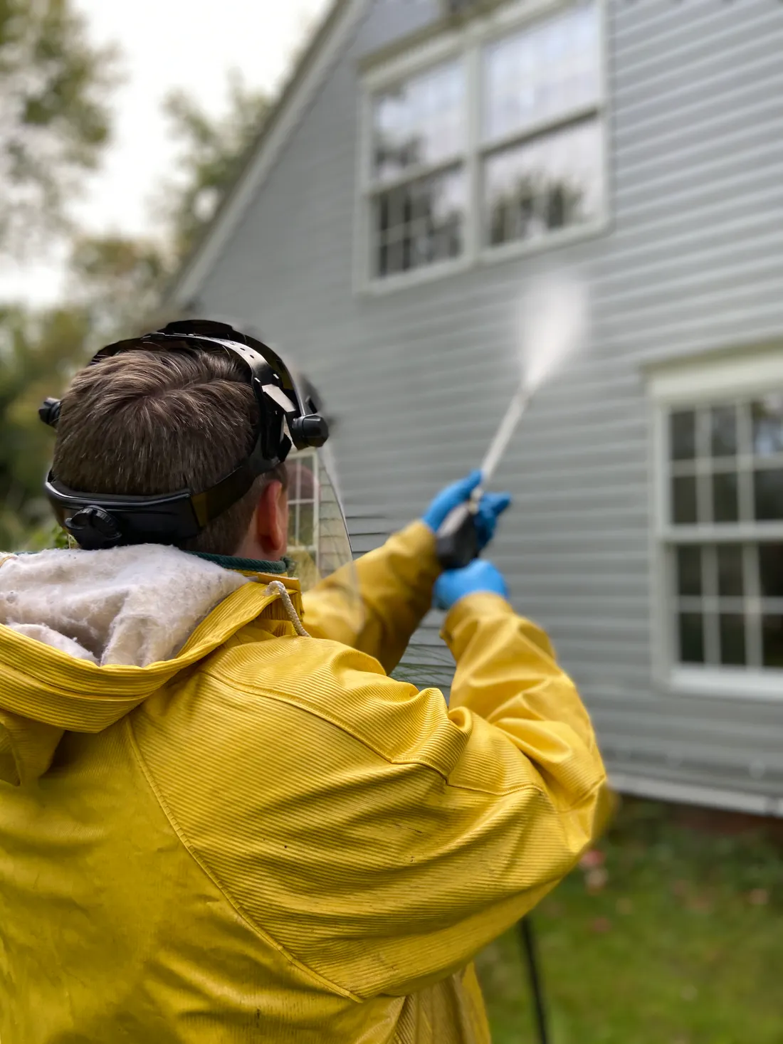 Siding being washed with a pressure washer wand, spray hitting the lap siding of a house